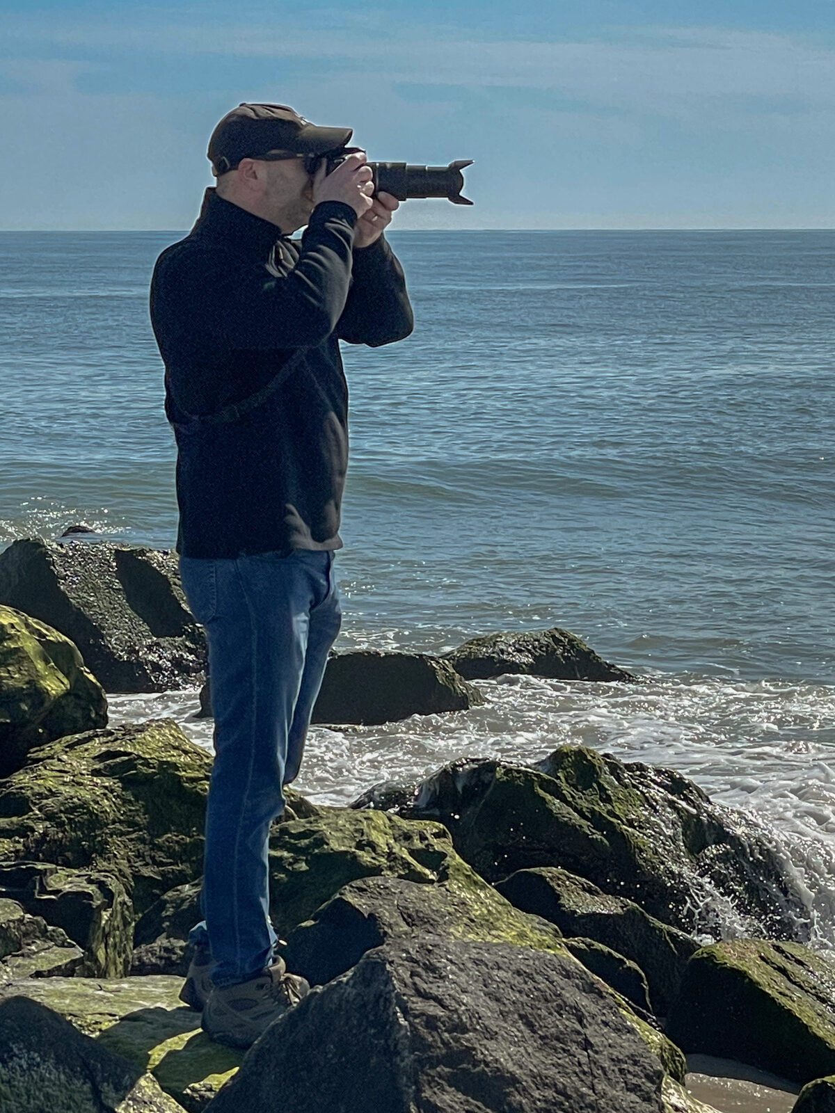 Brad Balfour standing on coastal rocks taking photos of the surf
